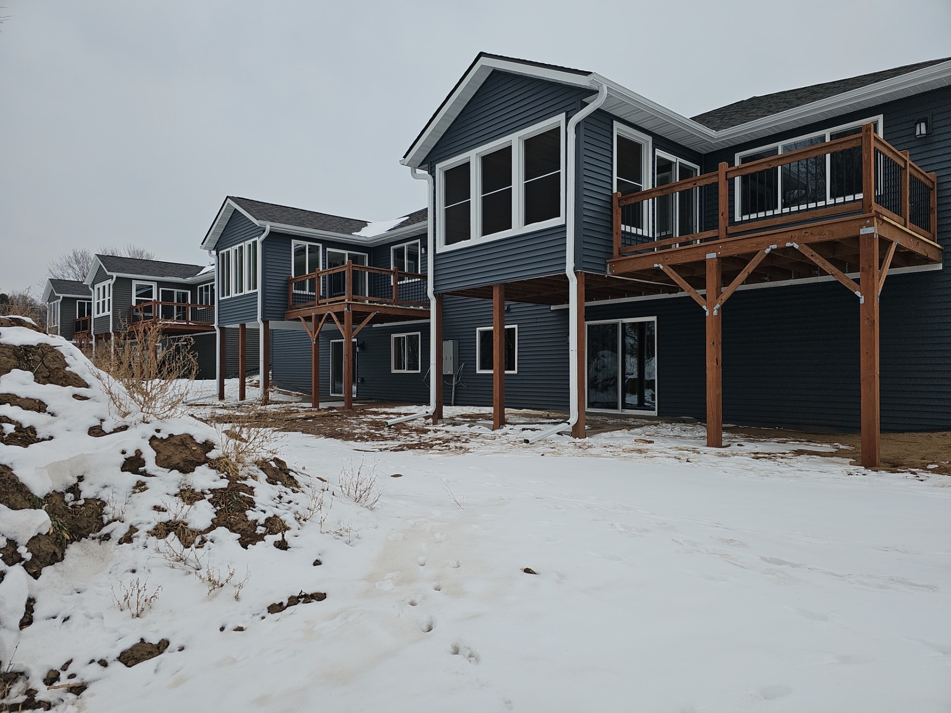 Row of newly built dark-blue custom homes with raised wooden decks and snow-covered ground, showcasing Claflin Construction's new construction and remodeling work in Eau Claire, WI.